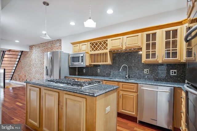 kitchen with a kitchen island, appliances with stainless steel finishes, glass insert cabinets, hanging light fixtures, and a sink