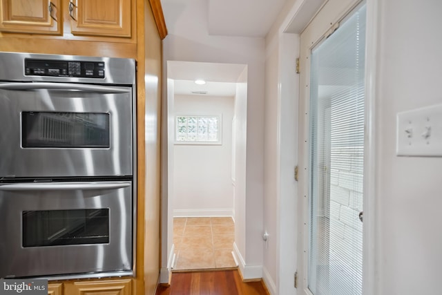 kitchen with double oven, light brown cabinets, baseboards, and dark tile patterned flooring