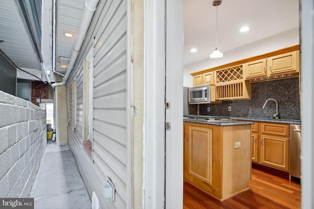 kitchen with wood finished floors, a sink, tasteful backsplash, stainless steel microwave, and decorative light fixtures