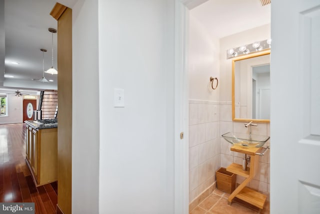 hall with a wainscoted wall, dark wood-style flooring, a sink, and tile walls