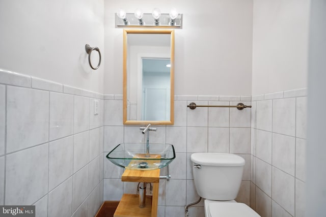 half bathroom with a sink, tile walls, and toilet