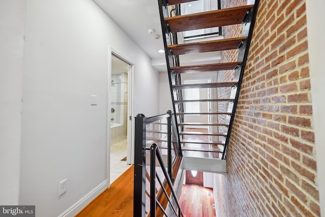 stairs featuring brick wall and wood finished floors