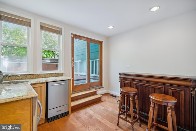 kitchen featuring light wood-style flooring, a sink, light stone countertops, stainless steel dishwasher, and recessed lighting