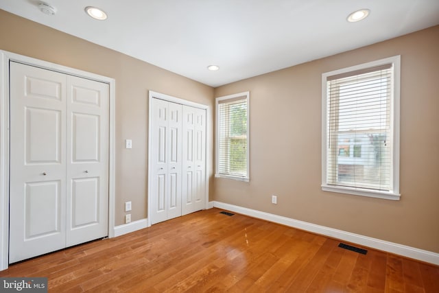 unfurnished bedroom with light wood-type flooring, baseboards, visible vents, and multiple closets