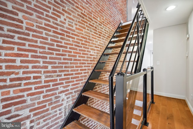 stairway with brick wall, baseboards, and wood finished floors