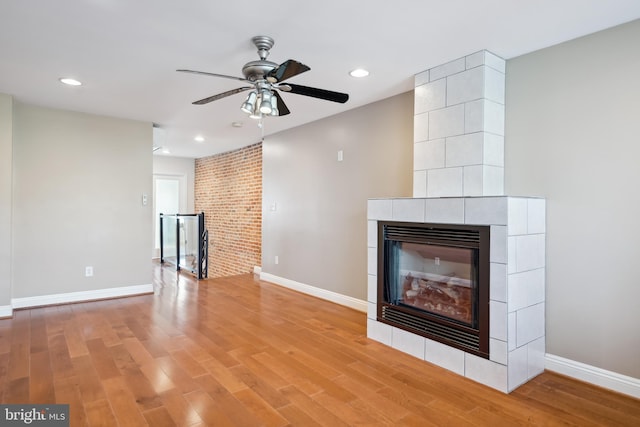 unfurnished living room featuring a tiled fireplace, baseboards, wood finished floors, and recessed lighting