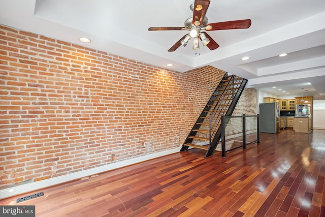 empty room featuring brick wall, dark wood-type flooring, visible vents, stairs, and a raised ceiling