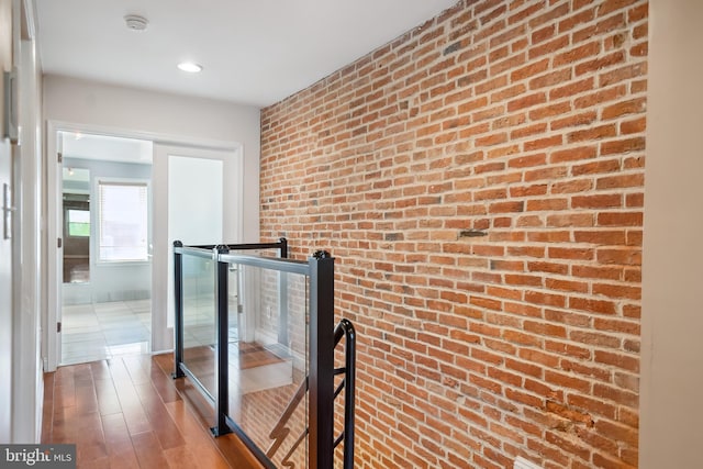 hall with brick wall, wood finished floors, and an upstairs landing