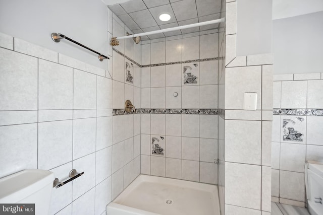 bathroom with toilet, tile walls, and tiled shower