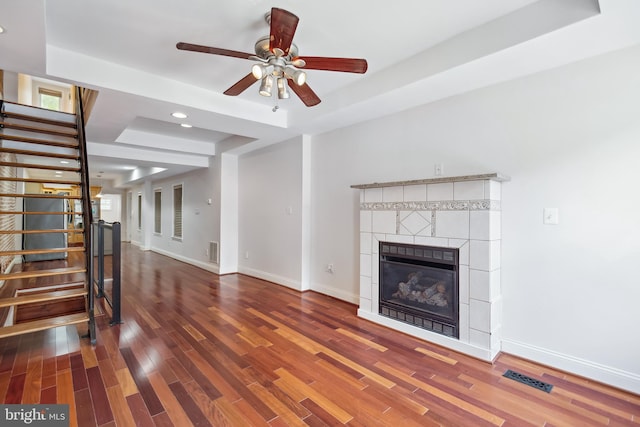 unfurnished living room with a fireplace, baseboards, stairs, dark wood-style floors, and a tray ceiling