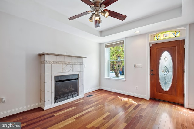 foyer featuring baseboards, a raised ceiling, a ceiling fan, wood finished floors, and a fireplace