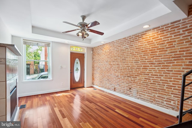 entrance foyer with a tray ceiling, visible vents, light wood-style floors, brick wall, and baseboards