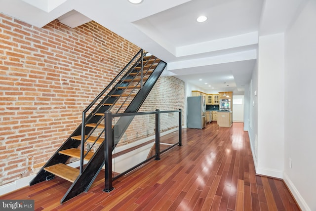 stairway featuring brick wall, baseboards, wood finished floors, and recessed lighting