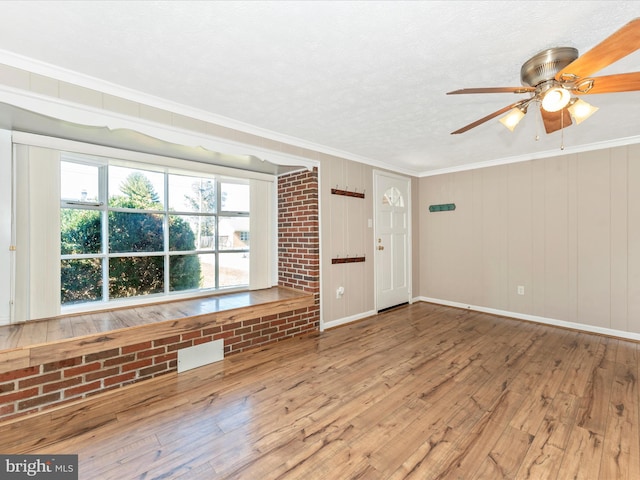 spare room with ornamental molding, wooden walls, ceiling fan, and hardwood / wood-style floors