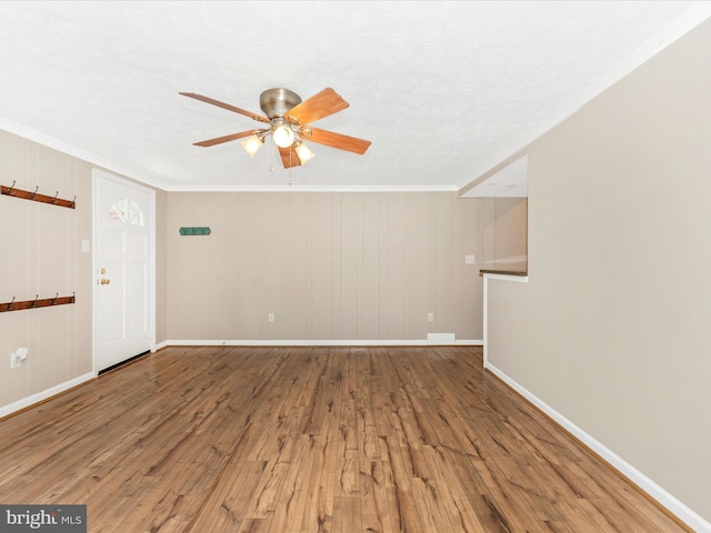 interior space with wooden walls, ceiling fan, hardwood / wood-style flooring, ornamental molding, and a textured ceiling