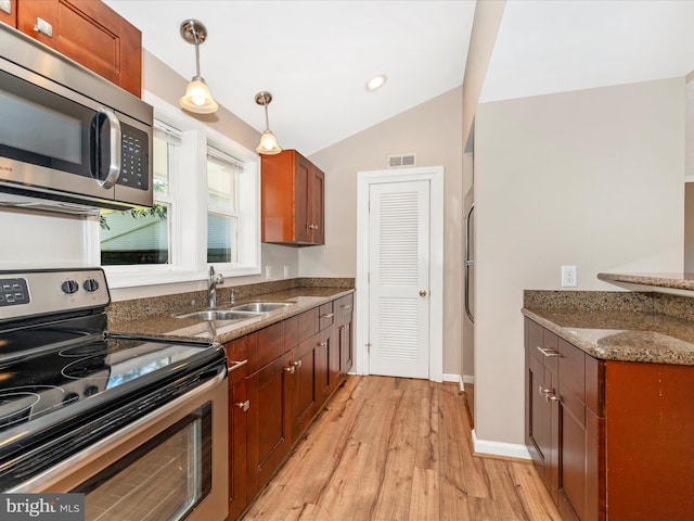 kitchen featuring vaulted ceiling, dark stone countertops, light wood-style flooring, stainless steel appliances, and a sink