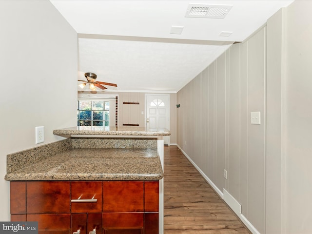 kitchen with light stone countertops, light hardwood / wood-style floors, wooden walls, and ceiling fan