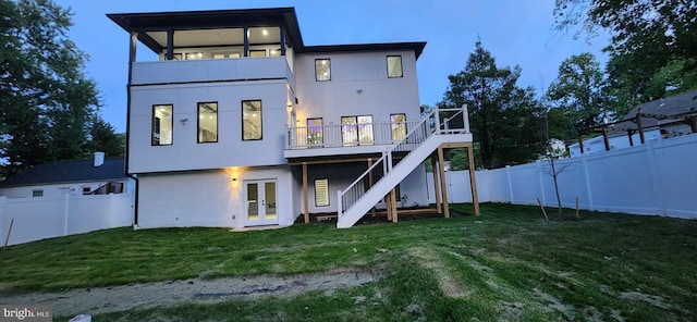 back house at dusk featuring a wooden deck and a lawn