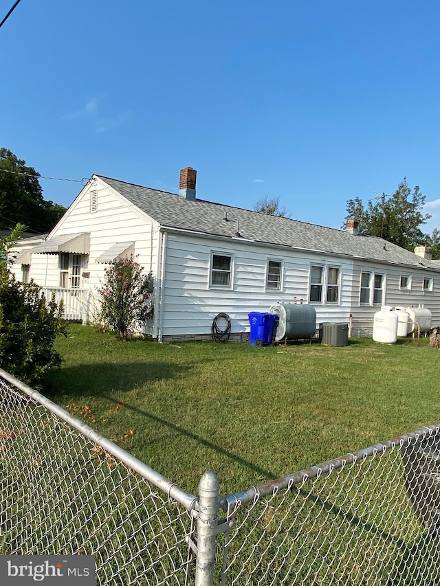 back of property featuring central air condition unit, a lawn, heating fuel, fence, and a chimney