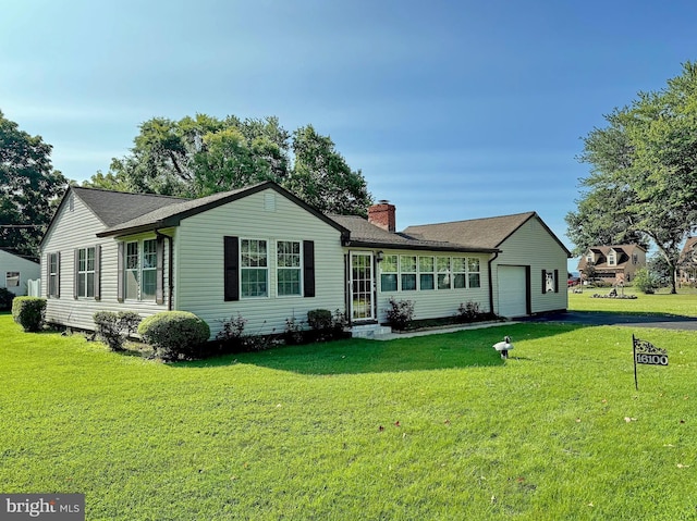 back of property featuring a garage, a shingled roof, a chimney, and a lawn