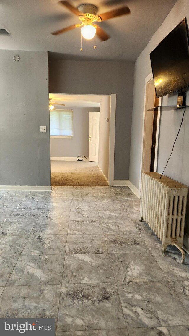 unfurnished room featuring ceiling fan, light tile patterned floors, and radiator