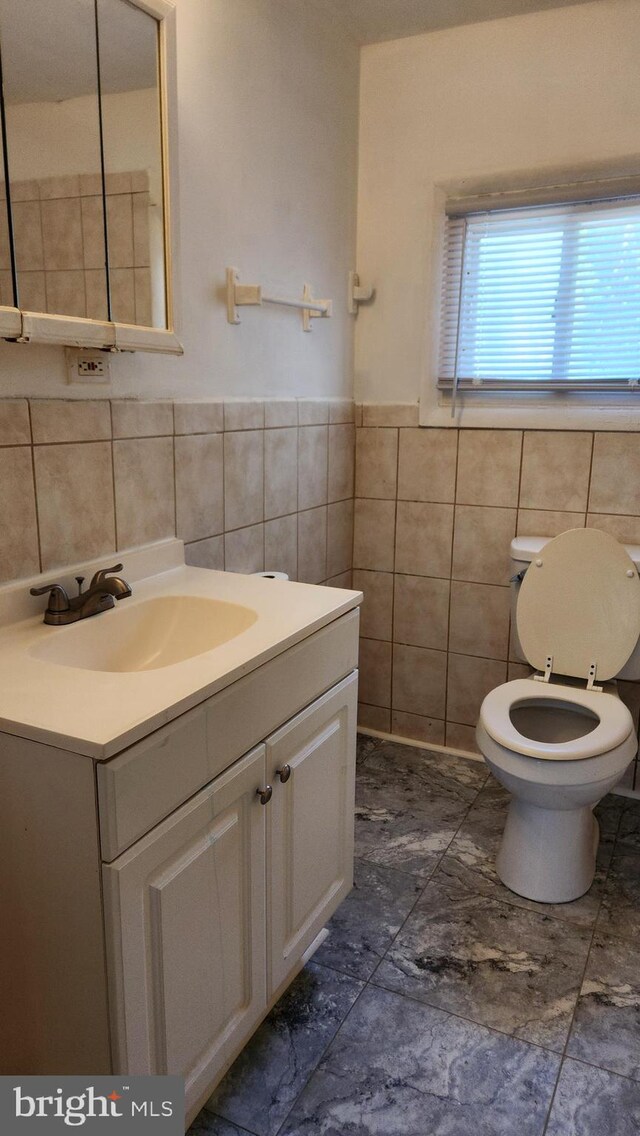 bathroom with toilet, tile patterned flooring, vanity, and tile walls