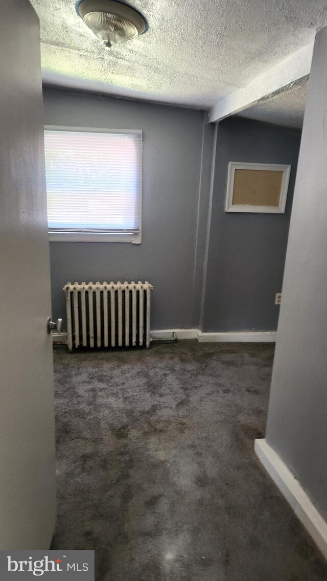 unfurnished room featuring carpet flooring, a textured ceiling, and radiator