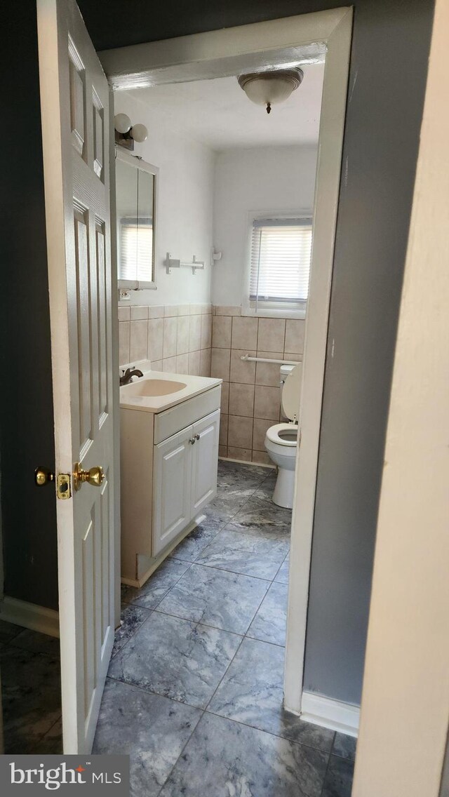 bathroom featuring tile patterned flooring, tile walls, toilet, and vanity