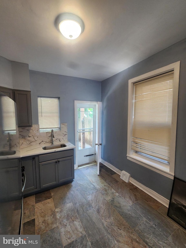 kitchen with sink, decorative backsplash, light stone countertops, and dark tile patterned flooring