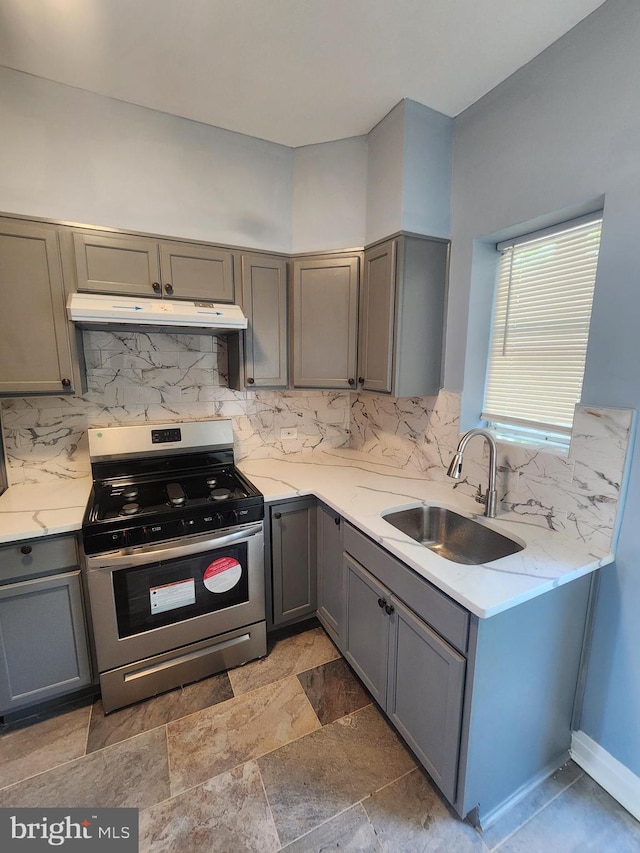 kitchen with gray cabinetry, gas range, light stone countertops, light tile patterned floors, and sink