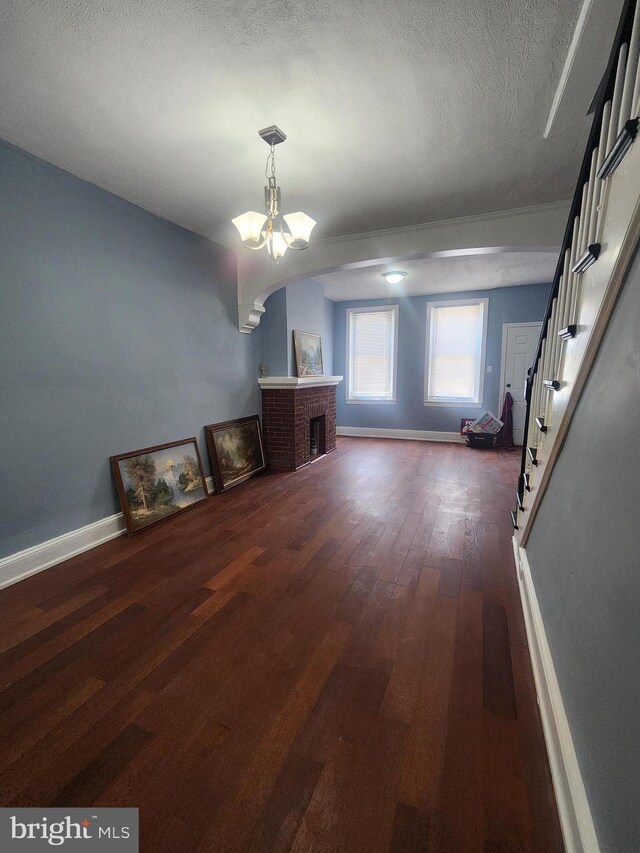 interior space featuring a textured ceiling, an inviting chandelier, dark wood-type flooring, and a brick fireplace