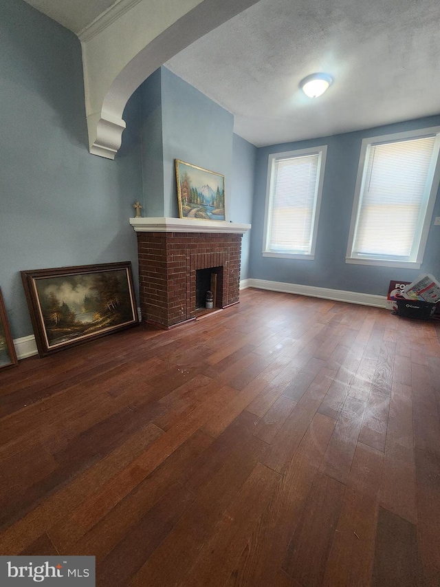 unfurnished living room featuring wood-type flooring, a textured ceiling, and a brick fireplace