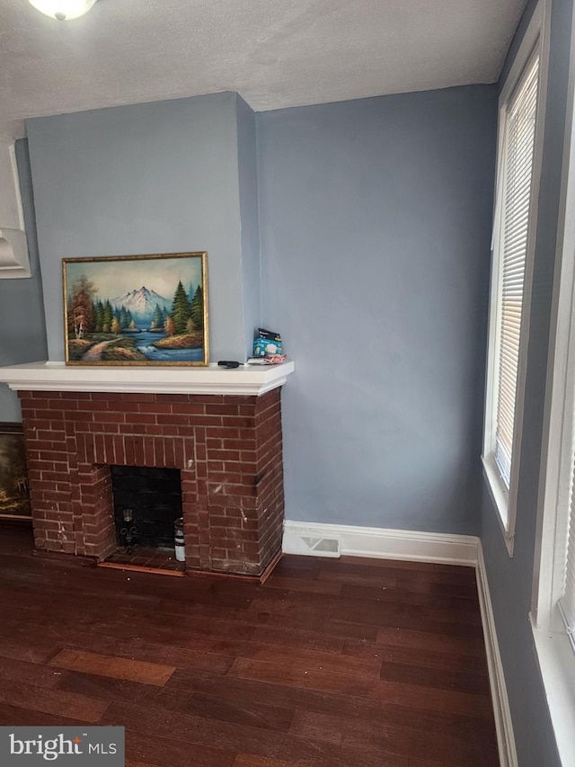 unfurnished living room featuring a textured ceiling, a brick fireplace, and wood-type flooring