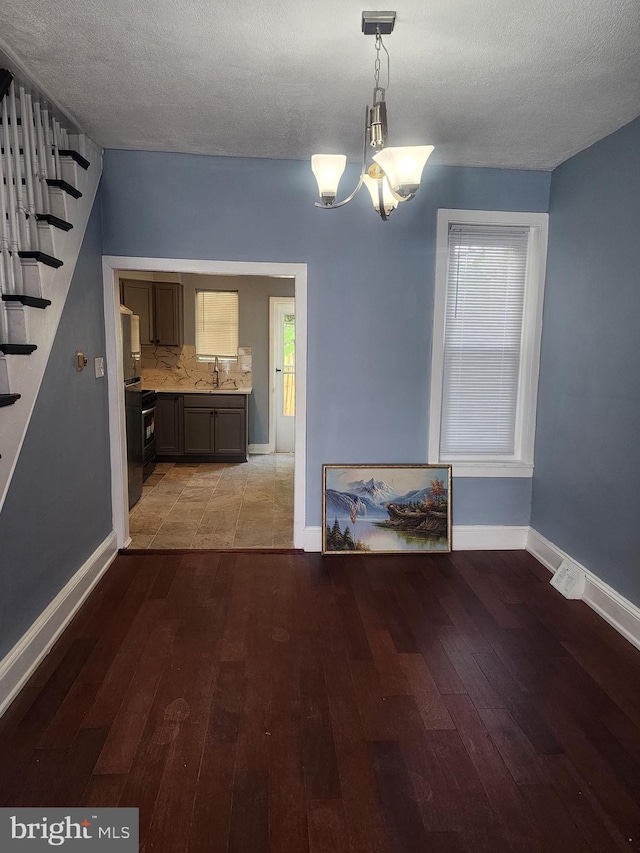 unfurnished dining area with light wood-type flooring, sink, an inviting chandelier, and a textured ceiling