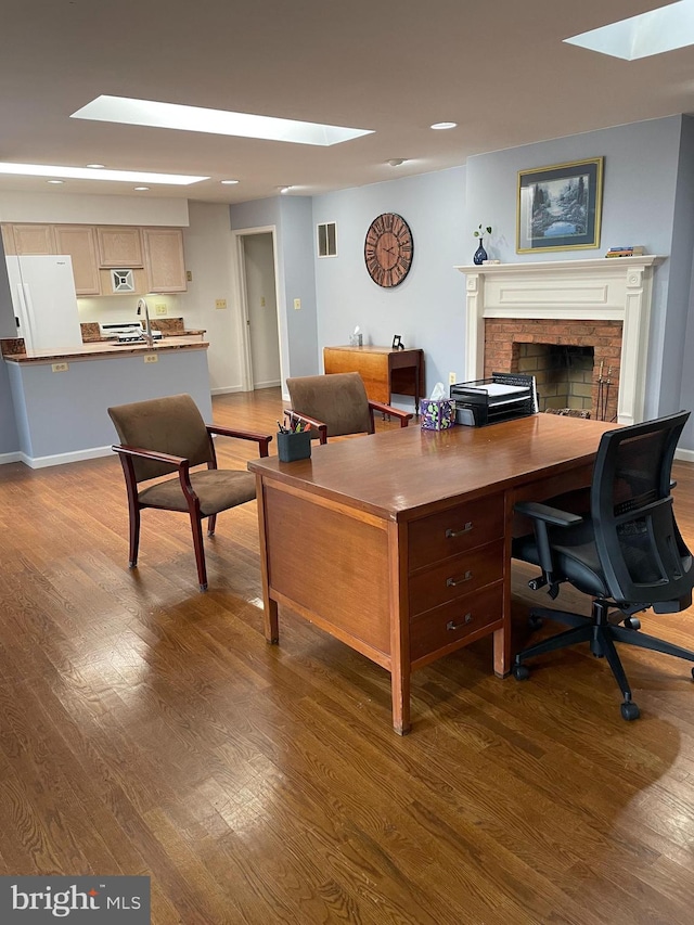 home office with hardwood / wood-style flooring, a skylight, a brick fireplace, and sink