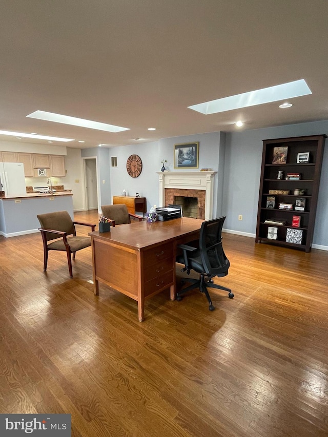 office featuring sink, a skylight, a brick fireplace, and hardwood / wood-style floors