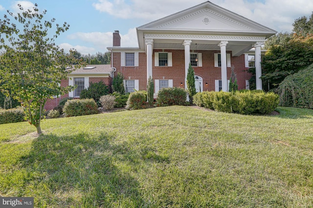 greek revival inspired property featuring a chimney, a front lawn, and brick siding