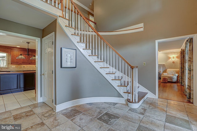 staircase with stone tile flooring, a towering ceiling, and baseboards