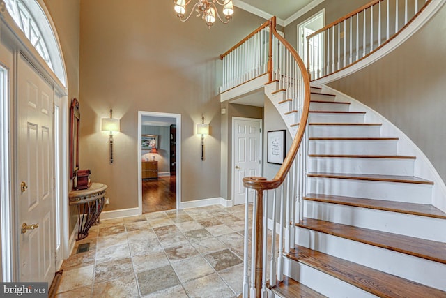 stairway featuring a high ceiling, baseboards, stone finish flooring, an inviting chandelier, and crown molding