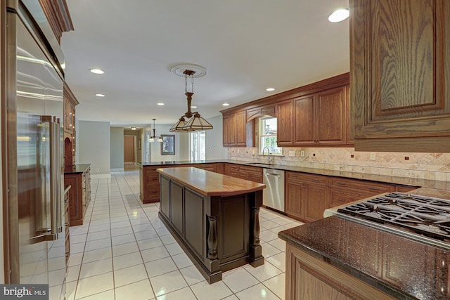 kitchen with light tile patterned flooring, a peninsula, stainless steel appliances, hanging light fixtures, and decorative backsplash