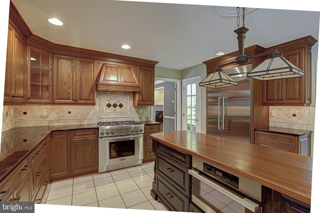 kitchen with high end appliances, decorative backsplash, butcher block countertops, custom exhaust hood, and light tile patterned flooring