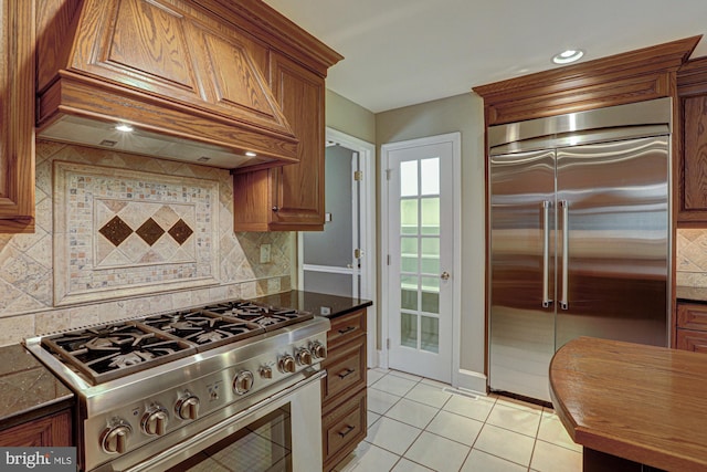 kitchen featuring light tile patterned floors, high end appliances, custom exhaust hood, and brown cabinets