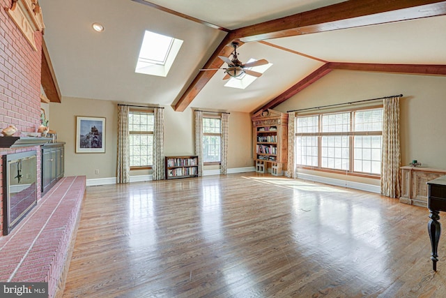 unfurnished living room featuring a ceiling fan, vaulted ceiling with skylight, baseboards, and wood finished floors