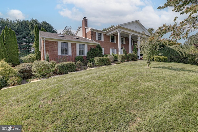 greek revival inspired property with covered porch, brick siding, a front lawn, and a chimney