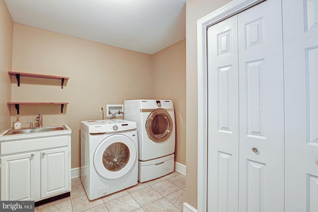 washroom with light tile patterned flooring, washing machine and dryer, a sink, baseboards, and cabinet space