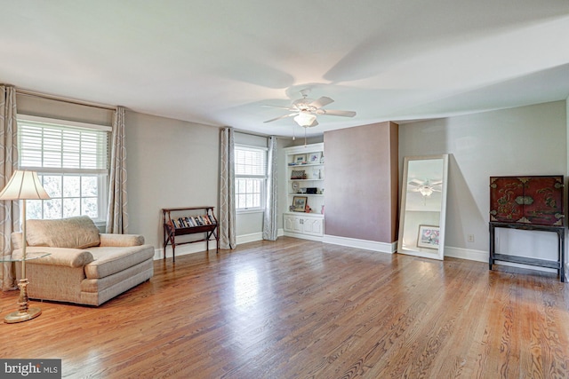 living area with ceiling fan, built in shelves, wood finished floors, and baseboards