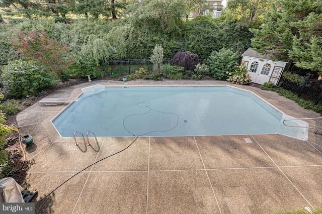 view of swimming pool featuring a fenced in pool, a patio, fence, an outdoor structure, and a diving board