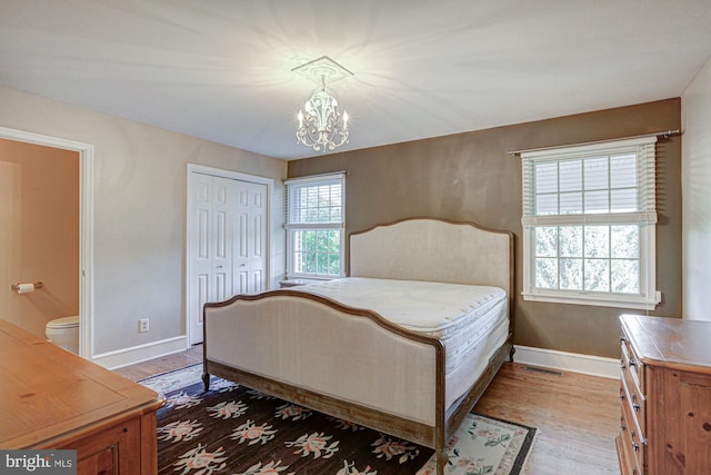 bedroom featuring a closet, visible vents, wood finished floors, a chandelier, and baseboards