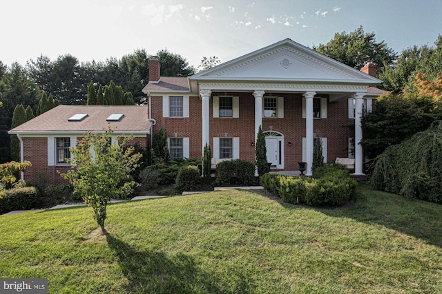 greek revival inspired property with a chimney, a front lawn, and brick siding