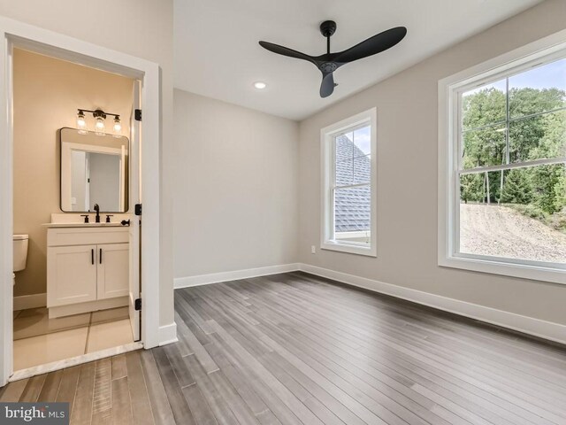 unfurnished bedroom with sink, ceiling fan, wood-type flooring, and ensuite bath